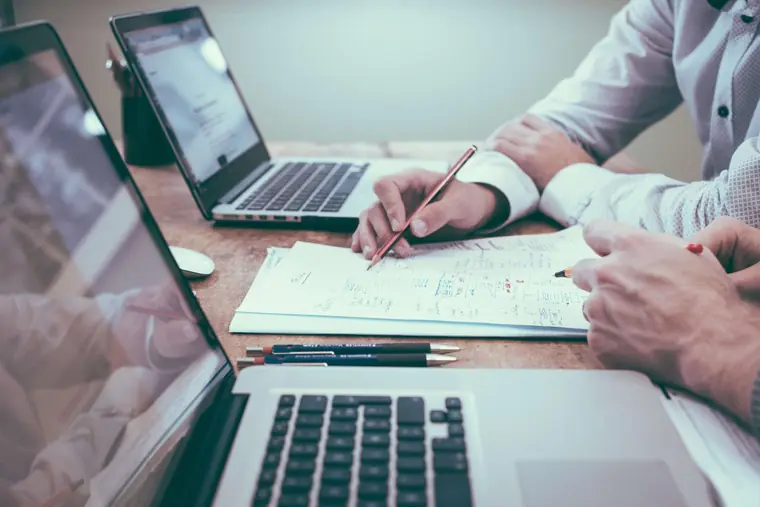 Duas pessoas revisando documentos e planilhas em uma mesa de trabalho
